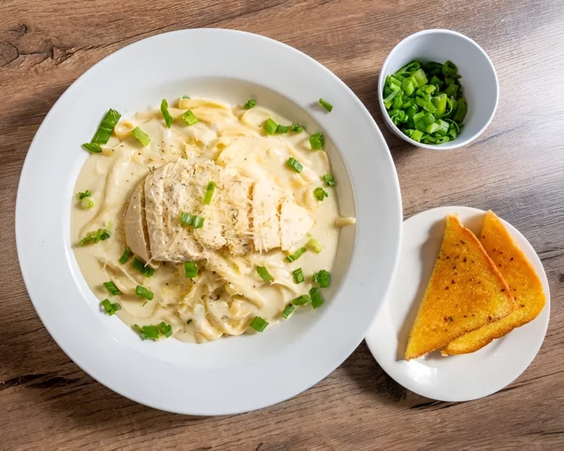 Creamy chicken pasta with green onions and garlic bread on a wooden table.