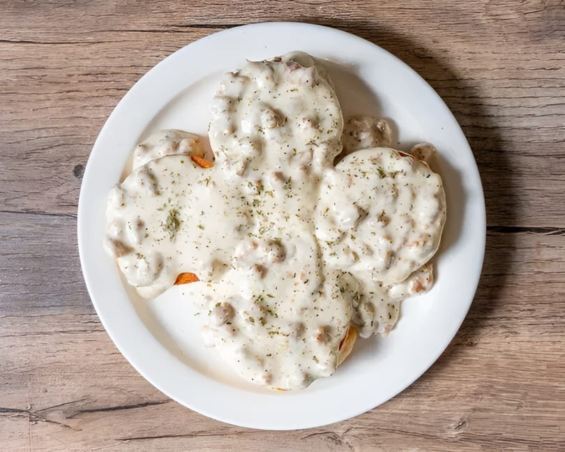 Biscuits and gravy on a white plate, topped with herbs, on a wooden table.